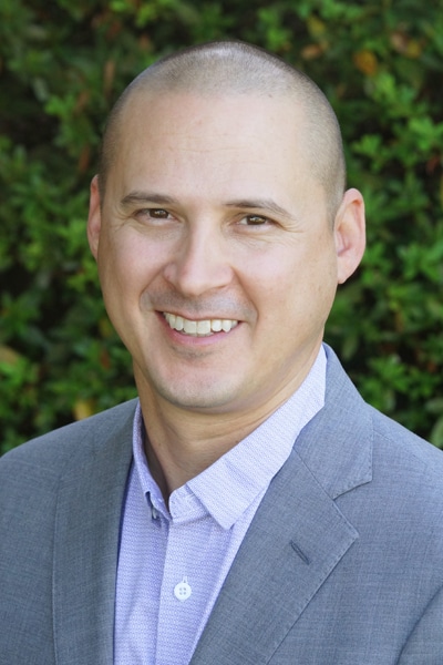 a man wearing a suit and tie smiling at the camera