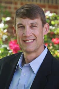 a man wearing a suit and tie smiling at the camera