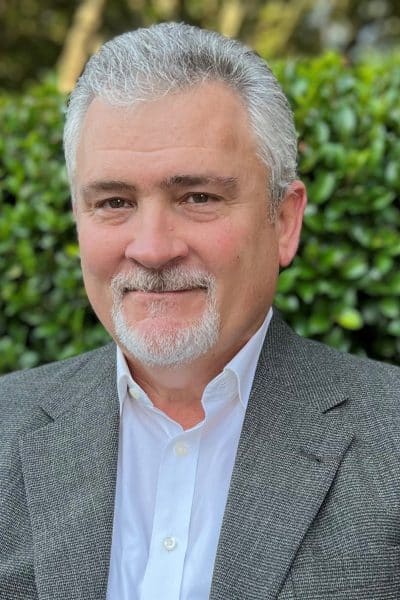 a man wearing a suit and tie smiling at the camera