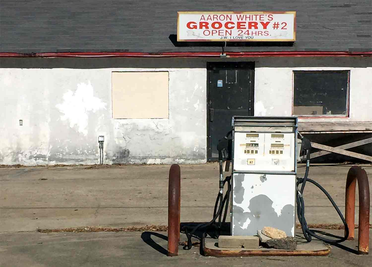 Front facade of the abandoned Aaron's Grocery building with peeling paint. Old fashioned fueling dispenser in disrepair in the foreground.