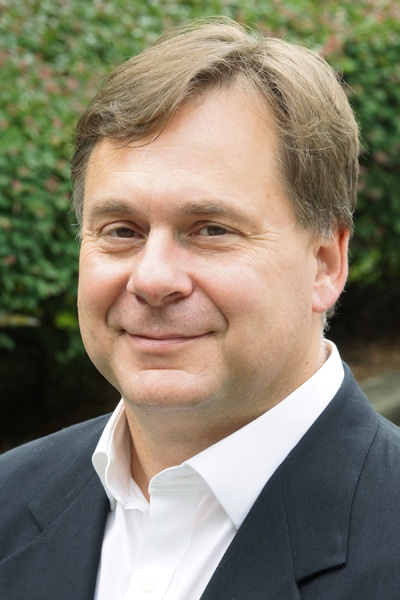 a man wearing a suit and tie smiling at the camera