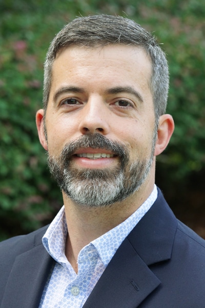 a man wearing a suit and tie smiling and looking at the camera