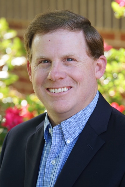 a man wearing a suit and tie smiling at the camera